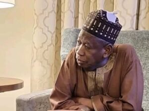 Abdullahi Ganduje seated indoors in traditional attire, looking contemplative.