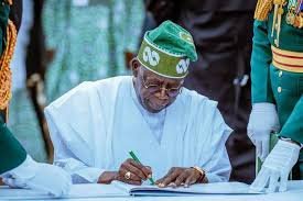 President Tinubu signing a document, with officials in ceremonial attire, as IMPI praises his economic reforms.