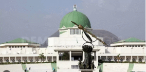 Front view of Nigeria’s National Assembly complex in Abuja with the green dome and the prominent legislative mace sculpture in the foreground.