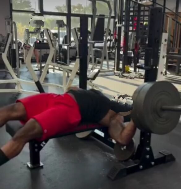A gym hall with weights on the floor as people gather around in shock after a young boy collapses during heavy lifting.
